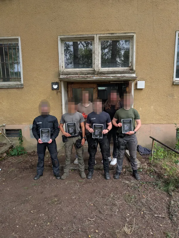 Teilnehmende eines früheren Lehrgangs mit Zertifikaten vor dem Ausbildungsgebäude